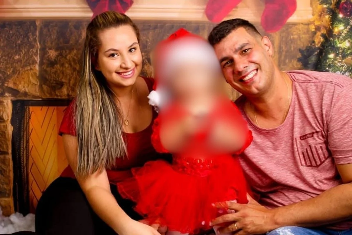 Foto colorida de casal posando com a filha ao centro da imagem.