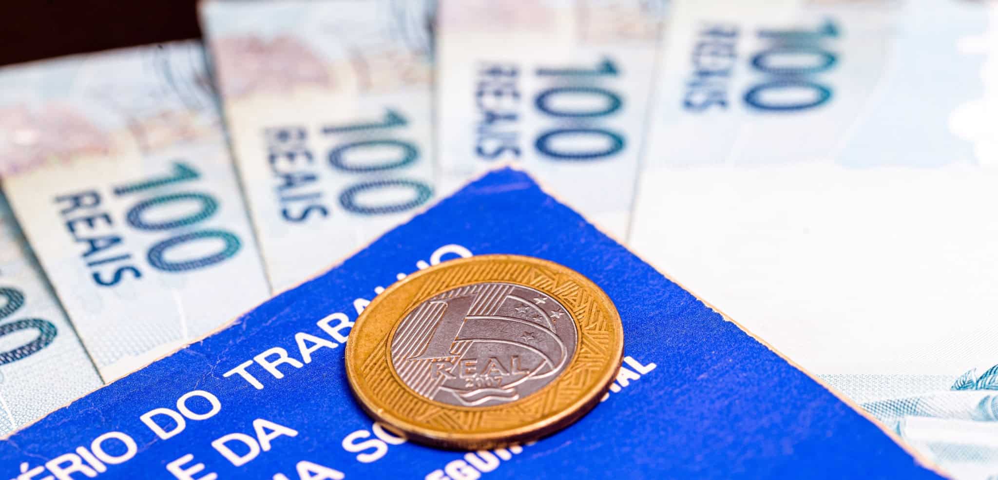 Notas de real com uma moeda e uma Carteira de Trabalho